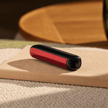 ملحق واجهة Ploom AURA الأمامية بلون أحمر بركاني مرفق بالجهاز على طاولة.
