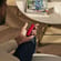 Man holding a Ploom device with a red back cover while sitting on a chair near a coffee table with magazines and a glass of water.